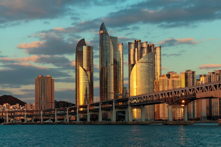 A stunning sunset view of the Busan skyline with bridge and skyscrapers reflecting sunlight.