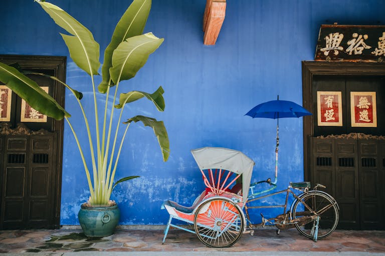 A vibrant rickshaw with umbrella against a blue wall, showcasing Malaysian heritage in George Town.