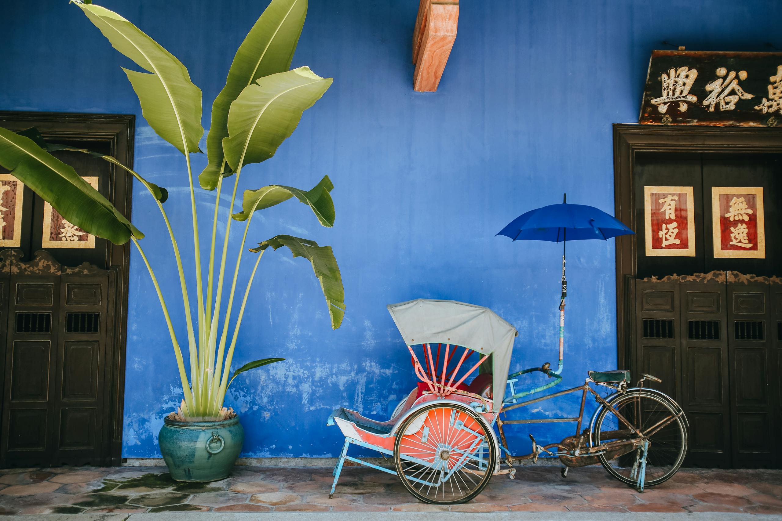 A vibrant rickshaw with umbrella against a blue wall, showcasing Malaysian heritage in George Town.