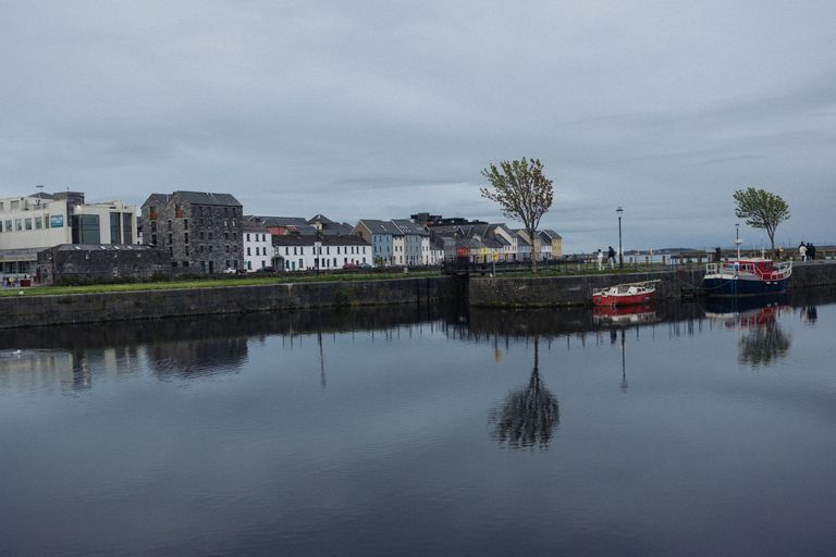 Serene harbor scene with colorful boats and historic buildings reflected in calm water.