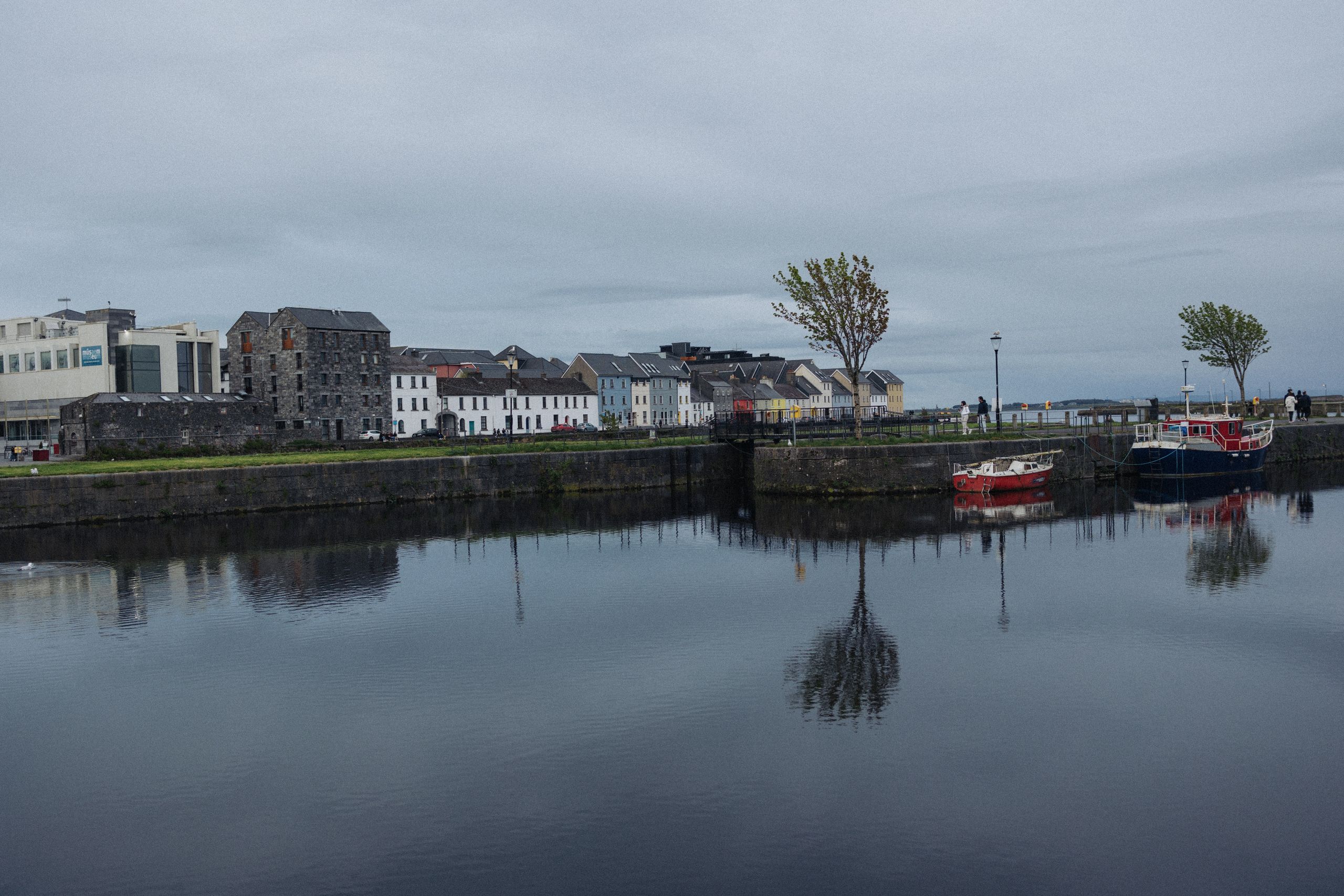 Serene harbor scene with colorful boats and historic buildings reflected in calm water.